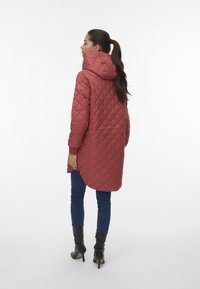 Gekwalte, gewatteerde jas in stofroze, met een langere achterkant, gestructureerd oppervlak en rib gebreide mouwen, gecombineerd met donkere denim en zwarte laarzen.