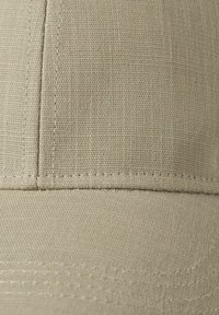 Beige tygbasebollkeps med en texturerad yta, med detaljerad sömnad längs sömmarna och en strukturerad krona.