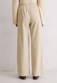 Beige Kordhosen mit weit geschnittenem Bein und elastischem Bund, die vertikale Rippstruktur und knöchellange Säume aufweisen.