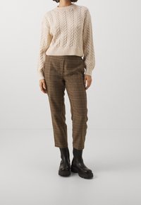 Krämfärgad kabelstickad tröja med ribbade manschetter, parat med bruna rutiga byxor. Bärs med svarta kraftiga anklarstövlar.