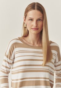 Beeži ja valged triibulised pika varrukaga särk laia kaelusega, kombineeritud kuldsete geomeetriliste kõrvaklappidega. Sile tekstuur ja mugav lõige.