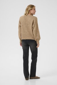 Pulover bej tricotat cu o croială lejere și tiv ribat, asortat cu blugi negri drepti și pantofi maro slip-on.