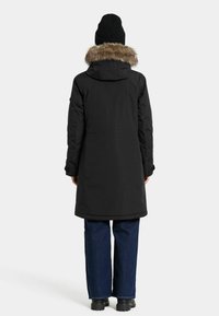 Zwarte lange parka met een met bont gevoerde capuchon, met een gladde textuur, aangesloten mouwen en zijzakken, gecombineerd met wijde jeans en een beanie.