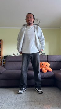 Haut à zip gris, t-shirt blanc, jean noir et baskets noires avec des accents blancs. Jouet en peluche pieuvre orange sur un canapé sombre en arrière-plan.