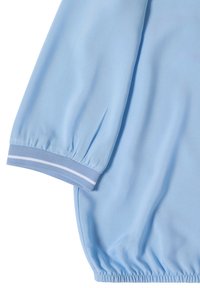 Chemise bleu clair à manches longues avec poignets et ourlet élastiques, avec une seule bande blanche sur le poignet.