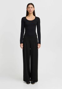 Černý dlouhý rukáv bodysuit s výstřihem do lodičky, doplněný černými širokými kalhotami. Tkanina je hladká, s přiléhavým vrškem a volným spodním dílem.