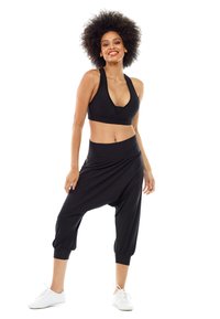 Top corto deportivo negro combinado con pantalones harem negros holgados, con una cinturilla y puños gathered, usados con zapatillas blancas.