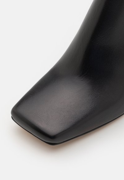 Black leather ankle boot with a square toe and a smooth texture, featuring a slim, elegant silhouette and no visible hardware.