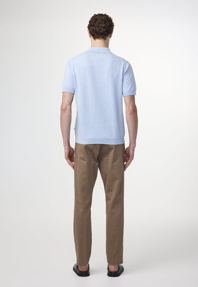 Vaaleansininen lyhythihainen pikeepaita, jossa on kaulus, yhdistettynä beigeihin suoriin housuihin ja mustiin liukuvaan kenkiin, nähtynä takaa.