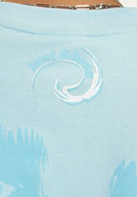 Light blue t-shirt with ribbed neckline, featuring a swirling white graphic and subtle blue brushstrokes on the back.