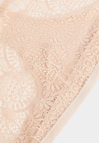 Tessuto di pizzo di colore pesca chiaro, con intricate fantasie floreali, delicati bordi ondulati e una morbida fascia elastica lungo il bordo inferiore.