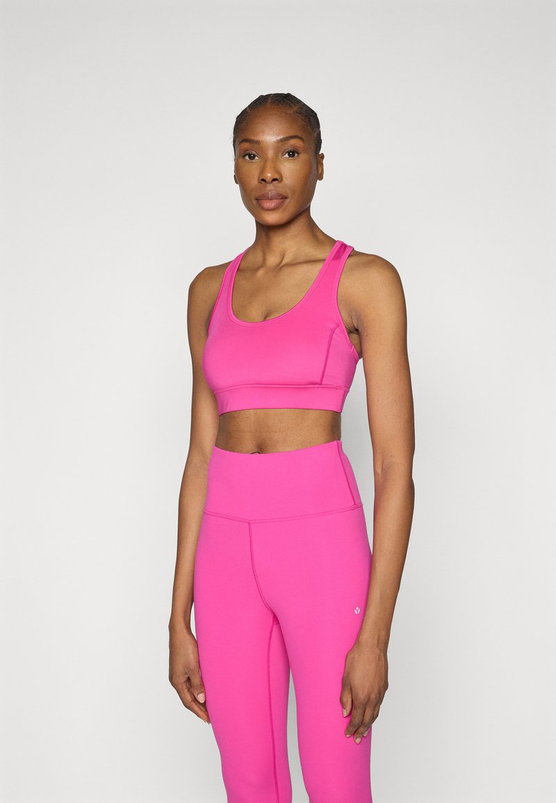 Top roz aprins și colanți din material elastic. Are un decolteu rotund și un design ajustat cu detalii de cusături contrastante.