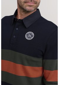 Mornaricki polo majica s horizontalnim prugama u zelenoj i narančastoj boji, izrađena od teksturiranog materijala. Ima ovratnik na gumbe i okrugli logo na prsima.