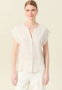 Camicia beige chiaro con strisce verticali multicolori, maniche corte, scollatura a V e bottoni sul davanti, realizzata in un tessuto testurizzato.