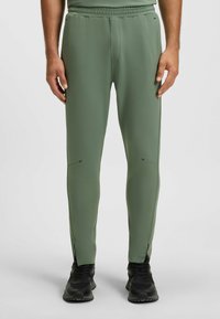 Green, fitted athletic pants with an elastic waistband, zippered accents at the ankles, and a smooth, sleek surface. Suitable for sports.