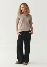 Haut beige clair à manches courtes avec un encolure en V et un tricot texturé, associé à un pantalon noir ample avec une taille élastique et des poches latérales.