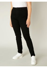 Zwarte skinny jeans gemaakt van denim, met een ritssluiting aan de voorkant, riemlussen en een strakke uitstraling, gecombineerd met witte sneakers.