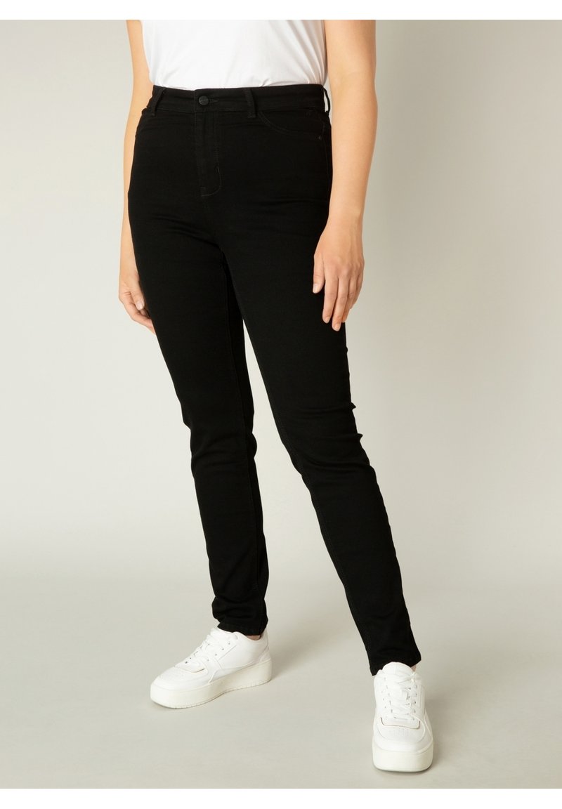 Zwarte skinny jeans gemaakt van denim, met een ritssluiting aan de voorkant, riemlussen en een strakke uitstraling, gecombineerd met witte sneakers.