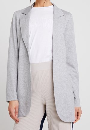 Cardigan grigio a maniche lunghe con colletto a scollatura, apertura frontale e tessuto morbido; indossato sopra una t-shirt bianca e leggings beige a coste.
