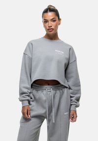 Felpa grigia cropped con maniche lunghe e polsini a coste. Presenta la scritta ricamata "GOOD FOR Nothing" sul petto. Tessuto morbido, vestibilità comoda.