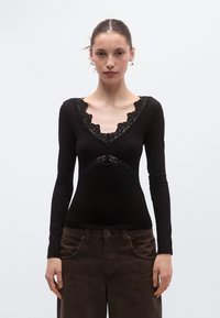 Μαύρο τοπ με μακριά μανίκια και δαντελένιες λεπτομέρειες στο ντεκολτέ και στη μέση. Διαθέτει εφαρμοστή γραμμή και απαλό ύφασμα.