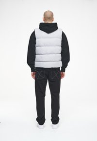 Grå pufferväst med horisontell kviltad design, som bärs över en svart hoodie. Svarta byxor och vita sneakers fulländar outfiten.