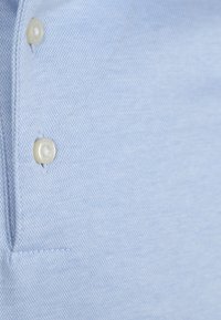 Lichtblauwe polo-shirt met een gestructureerde brei, voorzien van twee ronde witte knopen langs de sluiting en nette stiksels langs de naden.