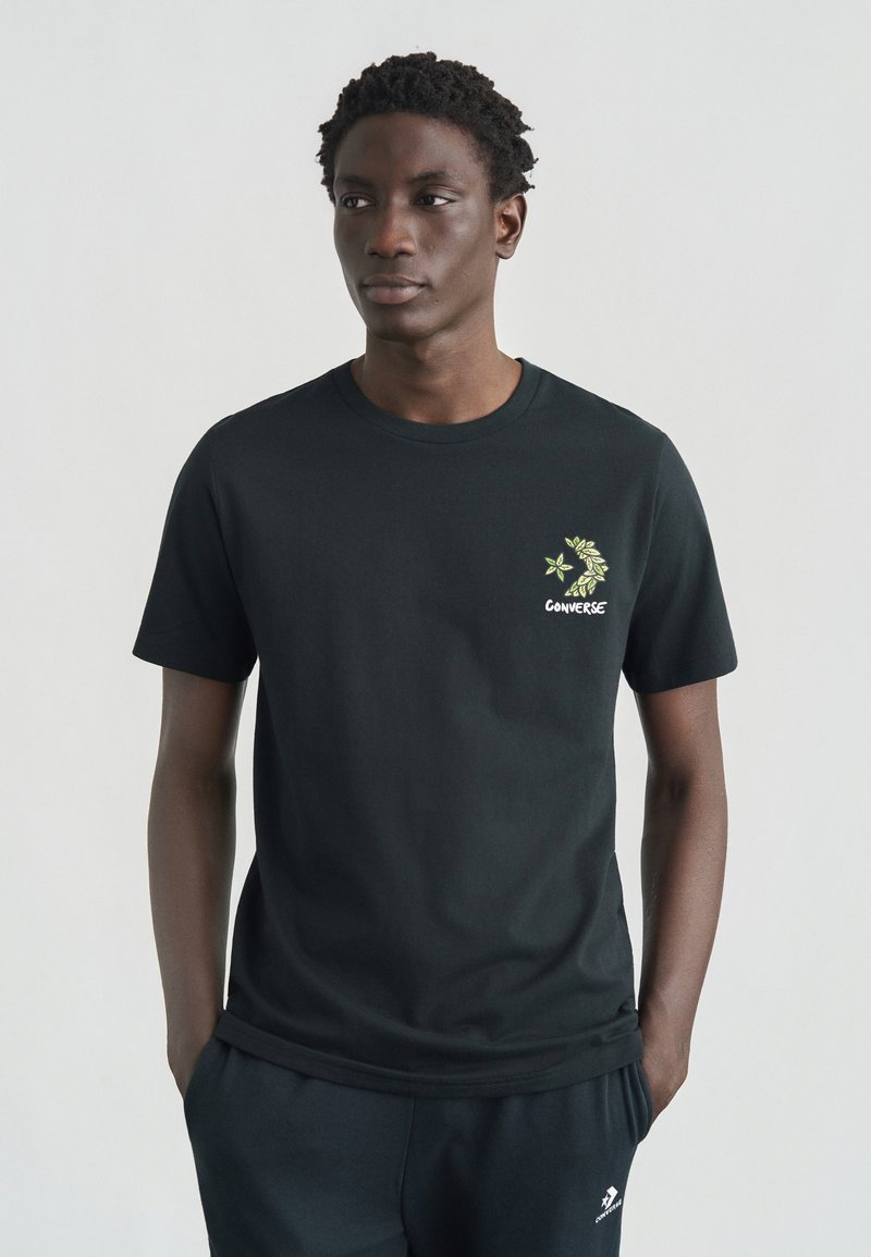 Μαύρο βαμβακερό μπλουζάκι με πράσινο λουλουδάτο σχέδιο και την επιγραφή "Converse" στο αριστερό στήθος. Κοντά μανίκια και στρογγυλή λαιμόκοψη.