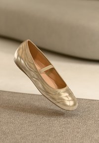 Goldenes Leder-Ballettschuh mit abgerundeter Zehe, strukturierten dekorativen Nähten und einem schmalen Riemen über dem Spann. Glattes Innenfutter.