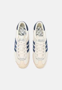 Zapatillas beige con rayas de ante azul marino, punta redondeada, diseño de cordones y plantilla con patrón. Parte superior de cuero texturizado y suela de goma.