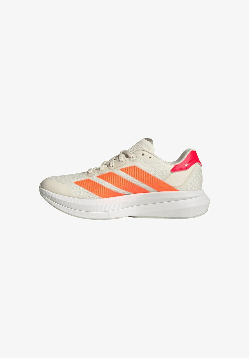 Chaussures de sport beiges avec tige en mesh, présentant trois larges bandes orange vives, un accent rose sur le talon, et une semelle blanche épaisse.