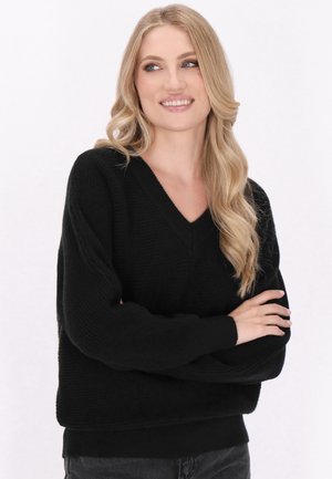 Maglione nero, texturizzato, con scollo a V e maniche lunghe. Presenta una vestibilità rilassata e polsini a costine, poggiando su uno sfondo chiaro.