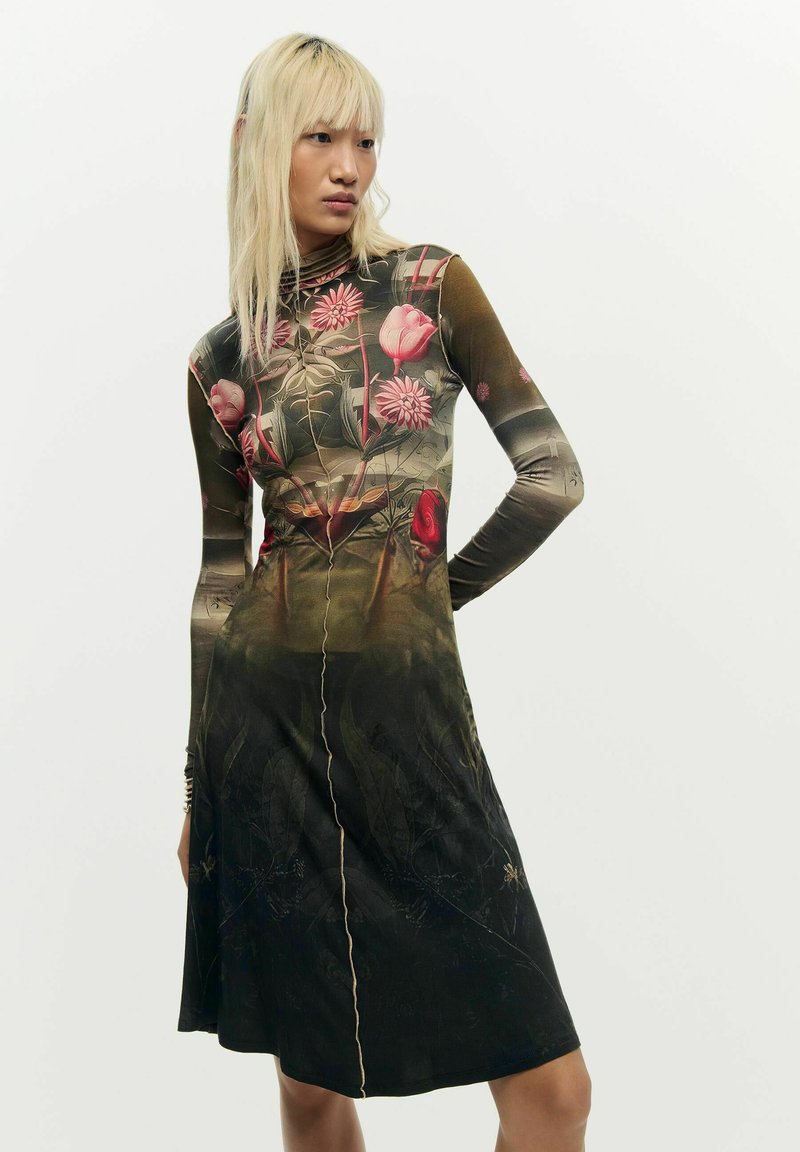 Persoană cu păr blond lung, purtând o rochie cu mâneci lungi, având un design floral închis cu flori roz și umbre degradate.