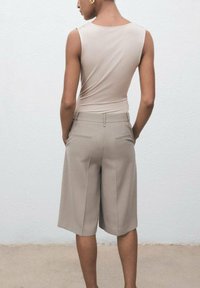 Top sin mangas color beige combinado con pantalones cortos beige de talle alto y corte ajustado, que llegan hasta la rodilla. Tejido suave con un sutil detalle de costura y bolsillos.