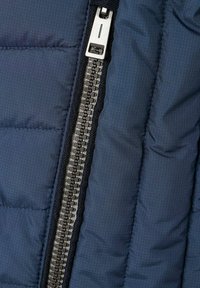 Lähellä otettu kuva hopeisesta metallivetoketjusta sinisessä tikkikankassa, jossa on ruutukuviota ja musta vetoketjun nauha.