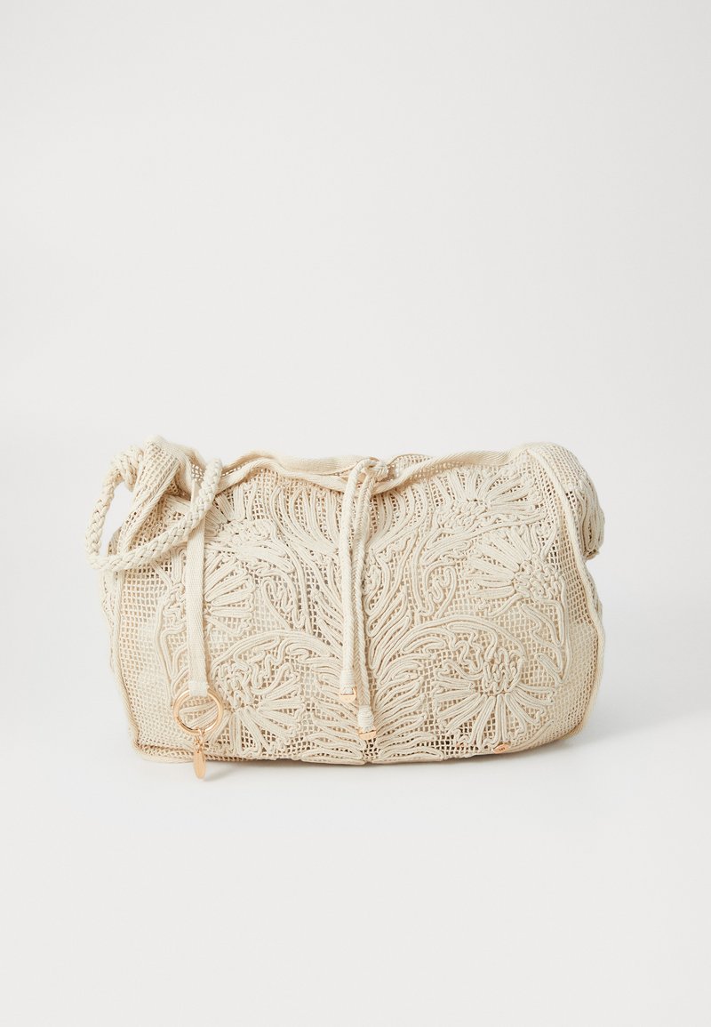 Cream-colored crochet handbag with floral patterns, drawstring closure, and braided shoulder strap on a white background.