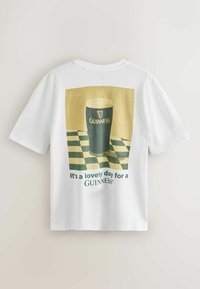 Biała koszulka z nadrukiem vintage szklanki piwa Guinness na kratkowanej powierzchni oraz tekstem "To piękny dzień na Guinnessa" na plecach.