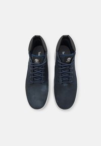 Tenisi din piele de culoare bleu marin, cu vârfuri rotunjite, talpă din cauciuc alb contrastant și șireturi asortate bleu marin. Logo-ul Timberland pe limbă.