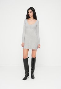 Γκρι πλεκτό φόρεμα με μακριά μανίκια, στρογγυλή λαιμόκοψη και λεπτομέρειες με κουμπιά. Συνδυασμένο με μαύρες δερμάτινες μπότες στιλέτο μέχρι το γόνατο.