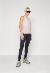 Light pink sleeveless tank top paired with dark leggings featuring textured patches, complemented by gray athletic shoes and black sunglasses.