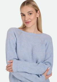 Jasnoniebieski sweter dziany o luźnym kroju, szerokim dekolcie i długich rękawach; charakteryzuje się miękką fakturą i prążkowanymi detalami.