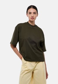 T-shirt oversize vert olive avec un col rond et des manches courtes, confectionné dans un tissu doux et lisse, offrant une coupe décontractée.