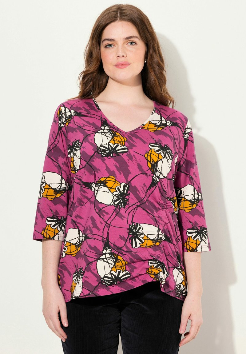 Tunika mit V-Ausschnitt in leuchtendem Lila mit einem floralen Muster in Weiß und Orange, ausgestattet mit Dreiviertelärmeln und einem abgerundeten Saum.