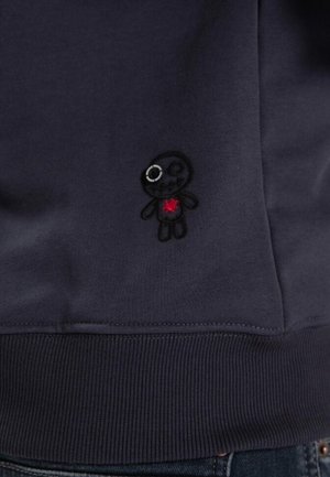Felpa di un blu navy scuro con un tessuto a trama. Design ricamato di un piccolo personaggio con un cuore rosso, dettagliato con un occhio lucido.