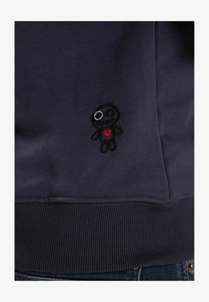 Felpa di un blu navy scuro con un tessuto a trama. Design ricamato di un piccolo personaggio con un cuore rosso, dettagliato con un occhio lucido.