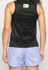 Černý síťovaný tílko s štítkem na zadní straně a světle fialové šortky s kontrastním bočním švem a hladkou texturou.