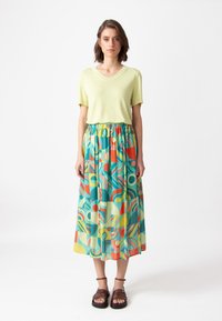 Lichtgroene V-hals top gecombineerd met een kleurrijke, patroon maxi rok met geometrische vormen in rood, teal, geel en wit.