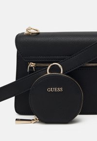 Svart handväska med textur och en avtagbar, cirkulär myntbörs. Gyldene detaljer och dragkedja på huvudfacket.