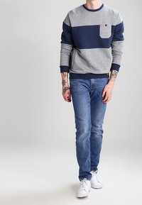 Grå och marinblå färgblockerad sweatshirt med rund hals, långa ärmar och ficka fram; matchad med blå jeans och vita sneakers.