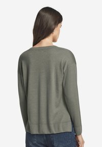 Olivgrön tröja med avslappnad passform, ribbad halsringning och nederkant, långa ärmar och mjukt tyg, sedd bakifrån.